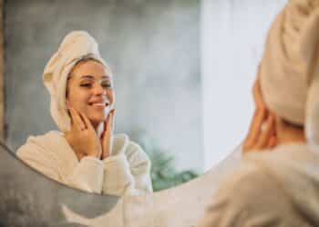 Mulher satisfeita observando resultados de skincare no espelho após rotina personalizada de cuidados