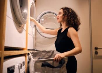 Mulher segurando sacola de lavagem próxima à máquina de lavar roupas moderna