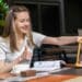 Mulher sorridente com ampulheta controlando tempo de estudo com livros e café na mesa