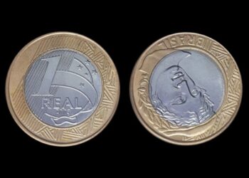 A imagem exibe a moeda de 1 real de 2003 com o erro de reverso invertido, mostrando o lado com o valor e o lado com a Efígie da República virado de cabeça para baixo.