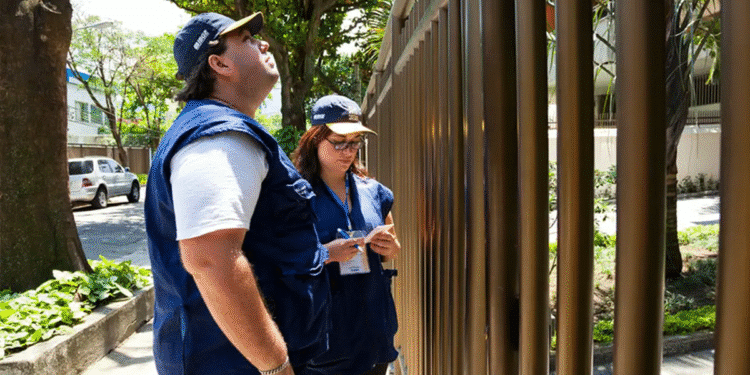 Equipe IBGE realizando pesquisa de campo em área residencial com pranchetas e uniformes oficiais