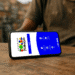Smartphone exibindo a tela inicial do aplicativo do Bolsa Família, com opções de acesso e informações sobre o programa, em uma superfície de madeira.