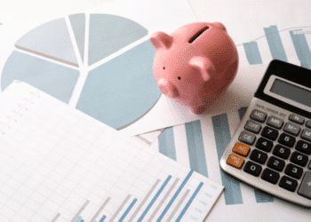 Mesa com um cofrinho, uma calculadora e gráficos de finanças, ilustrando o tema de economia e planejamento.