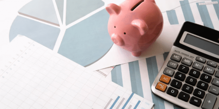 Mesa com um cofrinho, uma calculadora e gráficos de finanças, ilustrando o tema de economia e planejamento.