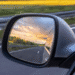 Reflexo de uma estrada e um pôr do sol com um cata-vento no retrovisor de um carro em movimento.