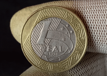 Moeda brasileira de R$ 1 de 1998 sendo segurada, mostrando o lado com a efígie da República e o ano de cunhagem.