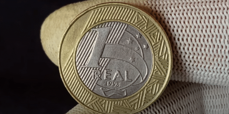 Moeda brasileira de R$ 1 de 1998 sendo segurada, mostrando o lado com a efígie da República e o ano de cunhagem.