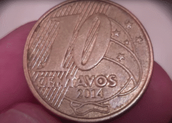 Uma moeda brasileira de 10 centavos do ano 2014, sendo segurada entre o polegar e o indicador, destacando a face da moeda com as palavras "10 CENTAVOS" e a data "2014".