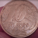 Uma moeda brasileira de 10 centavos do ano 2014, sendo segurada entre o polegar e o indicador, destacando a face da moeda com as palavras "10 CENTAVOS" e a data "2014".