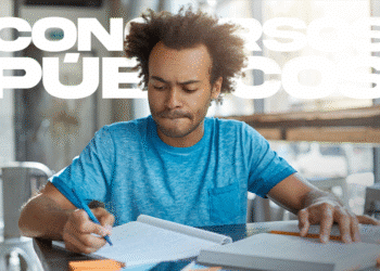 Homem concentrado em escrever anotações em caderno azul durante estudo para concurso público em ambiente iluminado