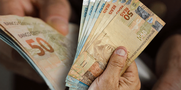 Pessoa segurando várias cédulas de R$ 50 com destaque para a data de saque do benefício