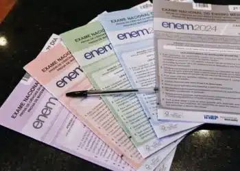 Cadernos e instruções do Exame Nacional do Ensino Médio (Enem) com caneta sobre mesa, com destaque para as cores dos cadernos de provas.