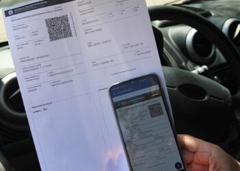 Documento CRLV impresso com QR code ao lado de celular mostrando versão digital dentro de carro