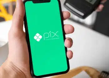Celular exibindo a logo do Pix em tela verde com uma maquininha de cartão no fundo, representando pagamentos digitais.