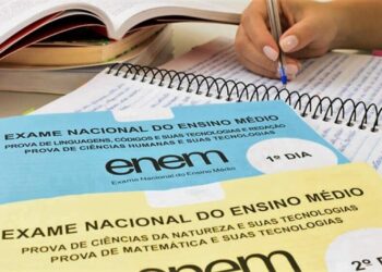 Estudante fazendo anotações com cadernos de prova do Enem sobre a mesa