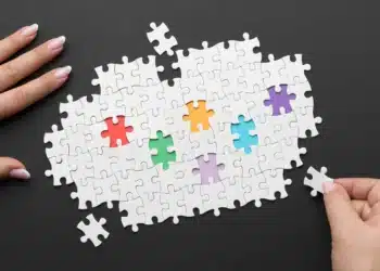 Imagem mostrando um quebra-cabeça com peças coloridas e uma mão segurando uma peça, representando a inclusão de jovens com TEA no programa de aprendiz do Bradesco.