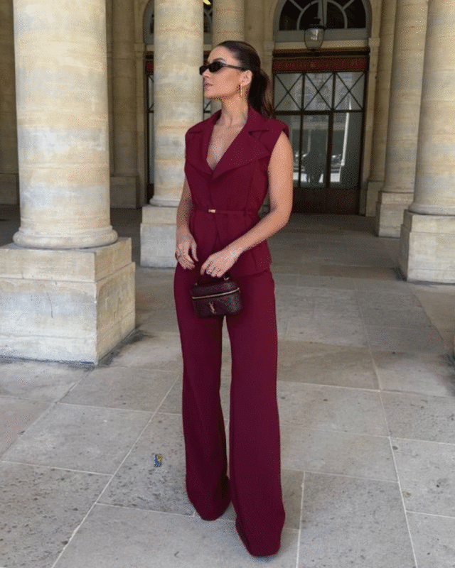 Mulher usando calça alfaiataria vinho, com blusa sem mangas, com cinto fino e óculos escuros em coluna clássica