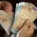 Pessoa segurando cédulas de 50 reais em pagamento de benefício.