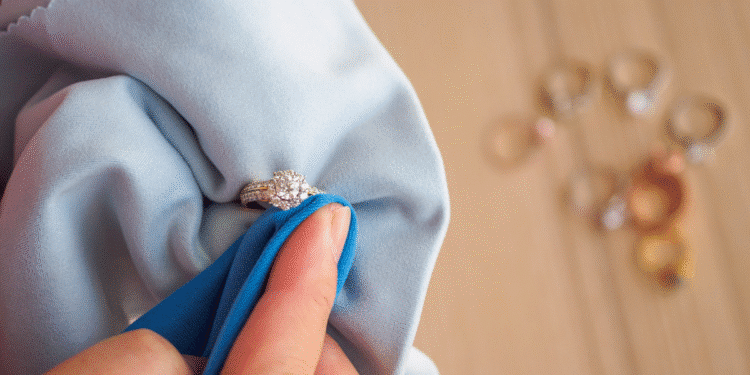 Pessoa limpando anel de diamante com pano azul suave, com outros anéis desfocados ao fundo.