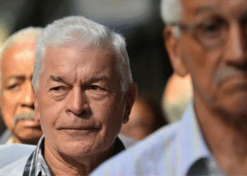 Grupo de homens idosos com expressão pensativa em um ambiente externo desfocado ao fundo