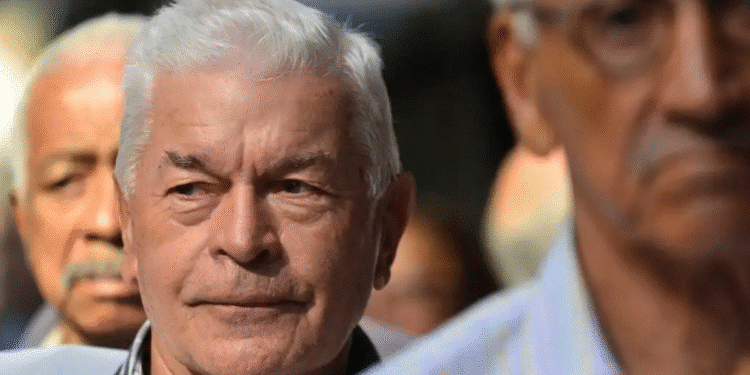 Grupo de homens idosos com expressão pensativa em um ambiente externo desfocado ao fundo