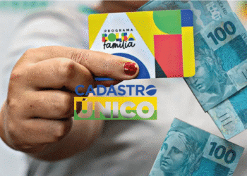 Cartão do programa Bolsa Família sendo segurado, com notas de 100 reais ao fundo e o logo do Cadastro Único, destacando a necessidade de atualização para continuar recebendo o benefício.