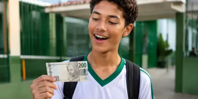 Estudante do ensino médio segurando nota de R$ 200 em frente a uma escola pública, representando o bônus do Pé-de-Meia para participantes do Enem 2026.
