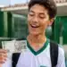Estudante do ensino médio segurando nota de R$ 200 em frente a uma escola pública, representando o bônus do Pé-de-Meia para participantes do Enem 2026.
