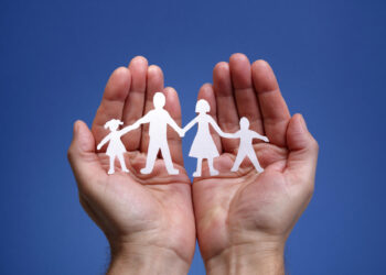 Papel cortado representando uma família sendo protegida pelas mãos, representando o seguro de vida.