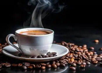 Xícara de café fumegante cercada por grãos de café frescos, com uma espuma suave sobre a bebida.