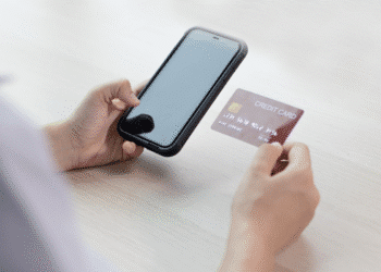 Mãos segurando celular e cartão de crédito para pagamento online na mesa clara