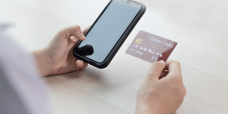 Mãos segurando celular e cartão de crédito para pagamento online na mesa clara