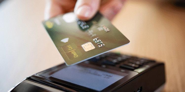 Mão segurando cartão de crédito próximo à maquininha para pagamento por aproximação