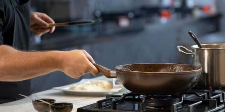 Mão segurando frigideira sobre o fogão em cozinha moderna, preparando comida para reduzir cheiro de fritura.