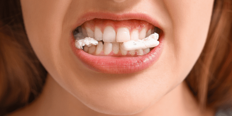 Close de boca feminina mordendo chiclete branco e dentes alinhados à mostra