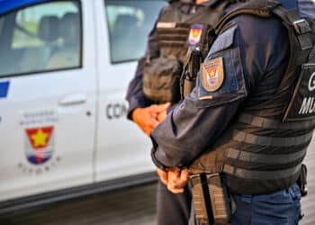 Guarda Civil Municipal de Vitória com uniforme preto e colete à prova de balas próximo a veículo oficial branco