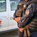 Guarda Civil Municipal de Vitória com uniforme preto e colete à prova de balas próximo a veículo oficial branco
