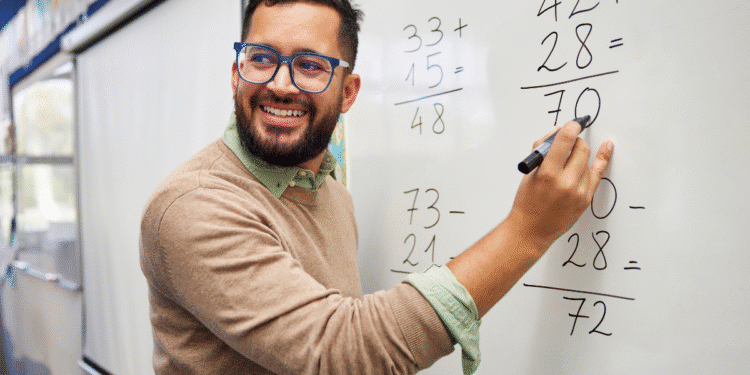 Professor sorridente resolvendo contas de soma e subtração em quadro branco em sala de aula