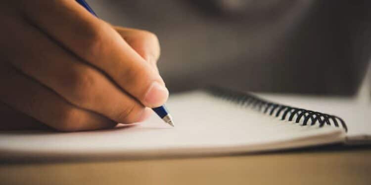 Pessoa escrevendo com caneta em caderno de espiral, preparando redação para o Enem