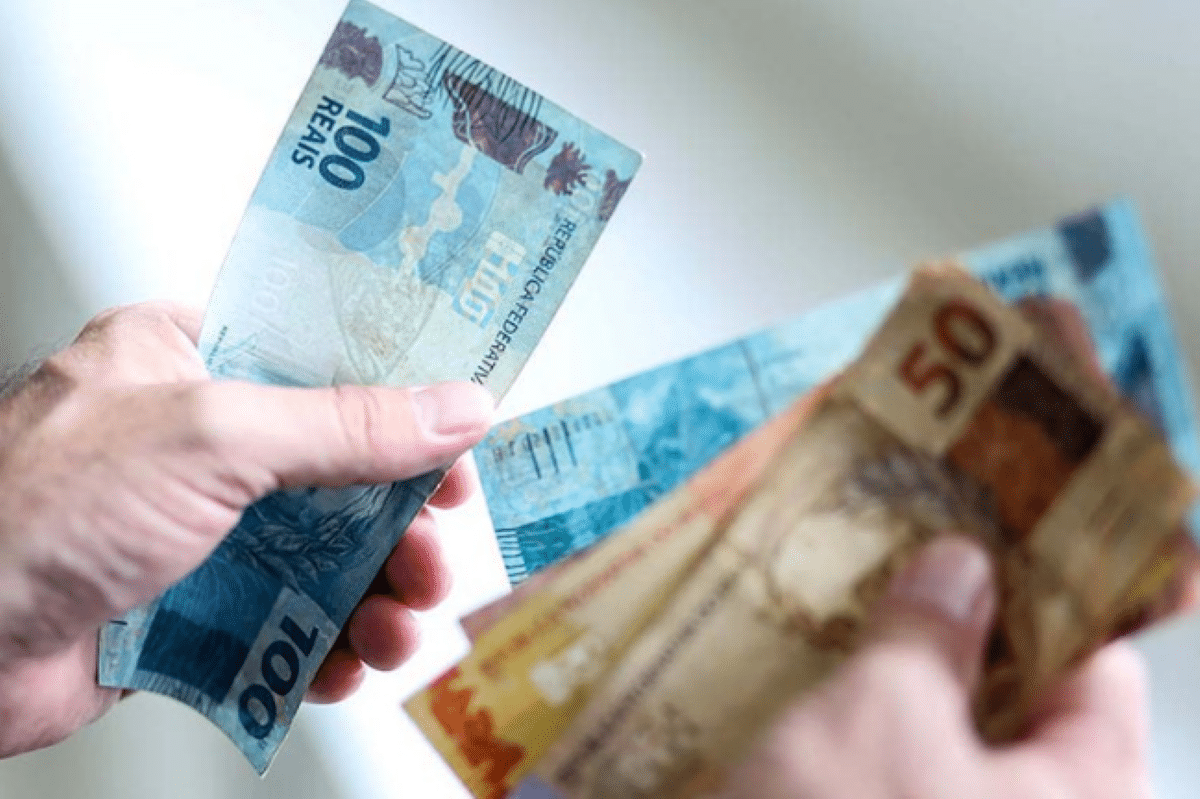 Imagem de mãos segurando notas de 100 e 50 reais com foco no pagamento do décimo terceiro para beneficiários do BPC/LOAS em 2025.