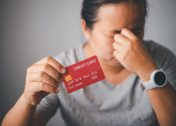 Pessoa preocupada segurando cartão de crédito vermelho, expressão de estresse financeiro