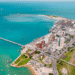 Imagem aérea mostrando o porto com prédios, cais e o mar azul ao redor