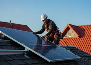 Pessoa instalando painel solar em telhado para aproveitar energia renovável.