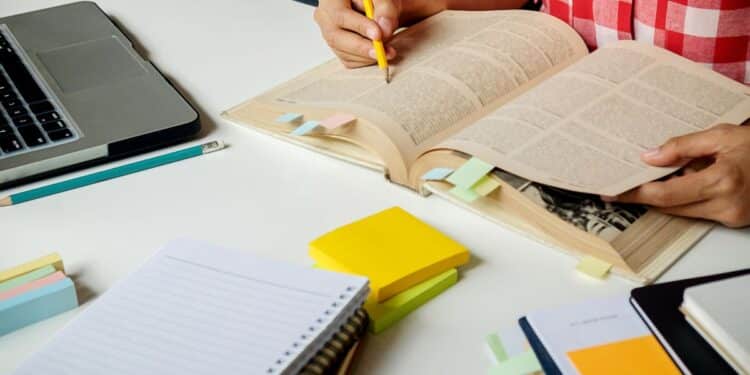 Pessoa estudando para concurso público com livros abertos, notebook e materiais organizados na mesa