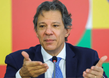 Homem de terno azul falando ao microfone diante de fundo colorido