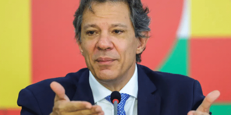 Homem de terno azul falando ao microfone diante de fundo colorido