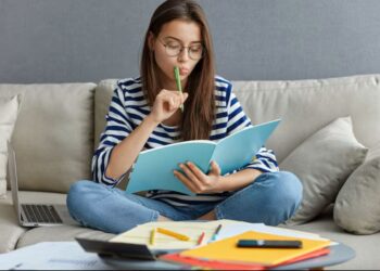 Jovem estudante focada revisando anotações para o Enem 2025, sentada em um sofá para ilustrar a memorização impulsionando os estudos.