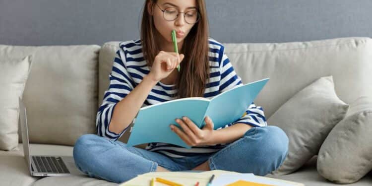 Jovem estudante focada revisando anotações para o Enem 2025, sentada em um sofá para ilustrar a memorização impulsionando os estudos.