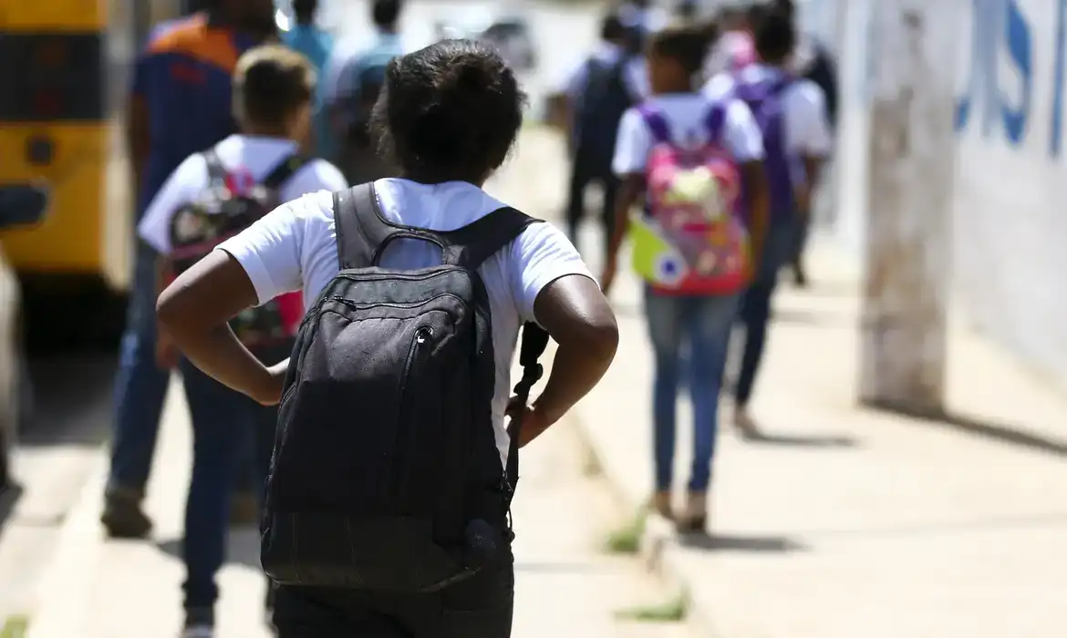 Frequência escolar exigida no Bolsa Família. Crianças caminhando para a escola com mochilas nas costas.