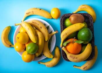 Vista superior de diferentes frutas, incluindo bananas e frutas cítricas, sobre uma superfície azul.